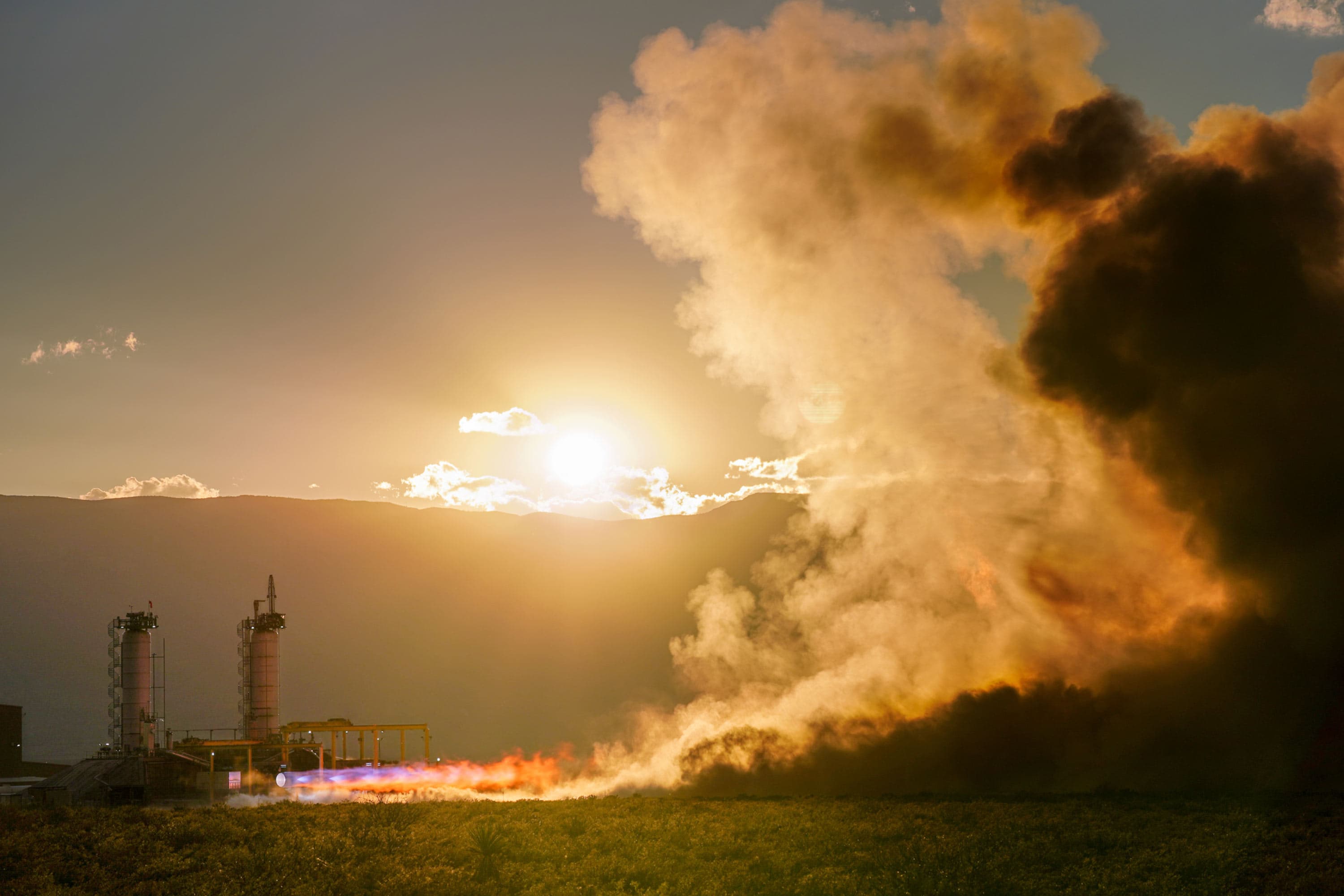 A Blue Origin BE-4 engine firing on a test stand at sunset.