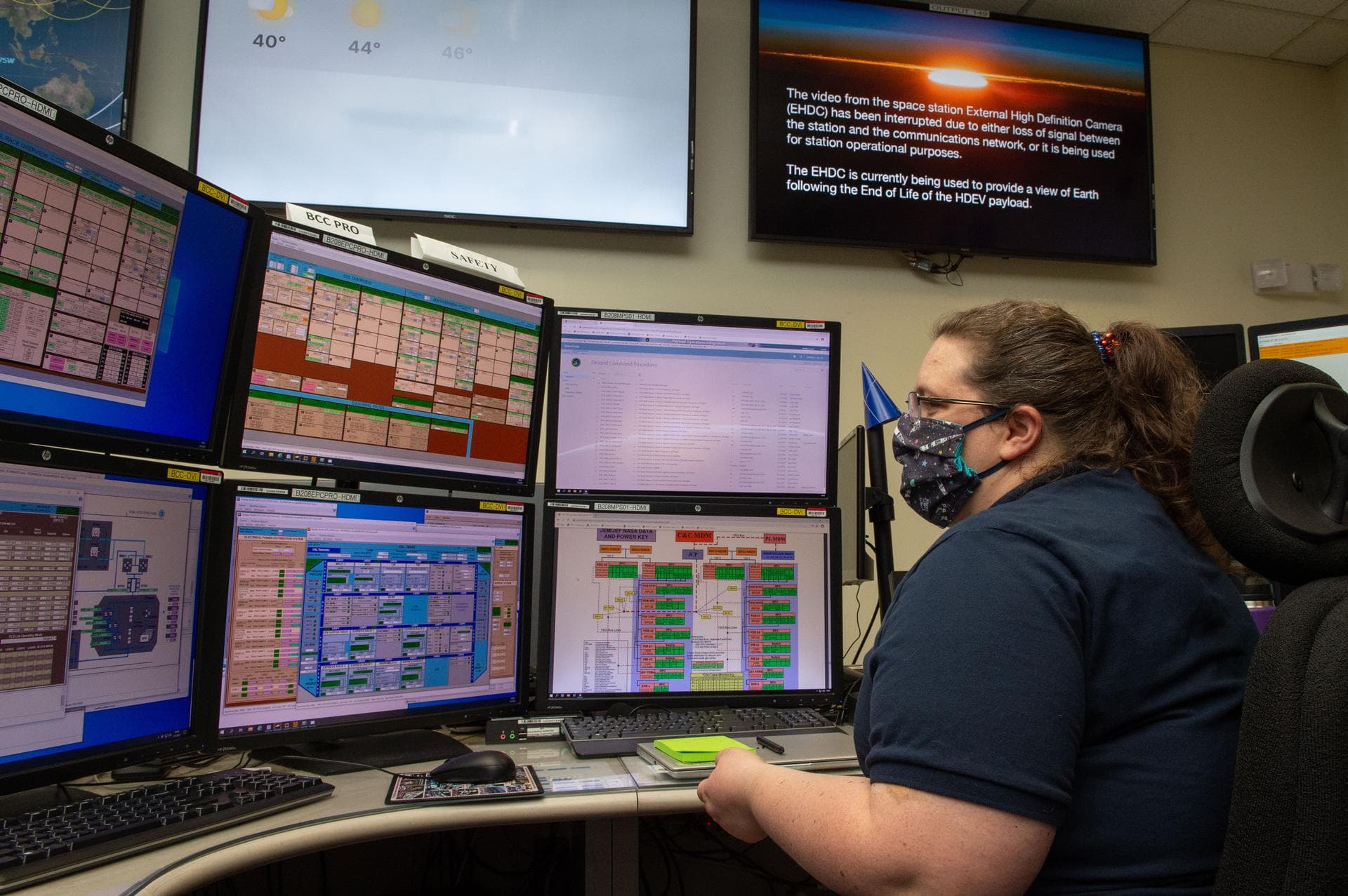 A mission-control operator monitors International Space Station systems on a bank of screens.